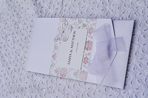 Image of Broderie Antique Rose long pocketfold invitation, decorated with flower and vine paper, organza bow , butterfly and gem. 