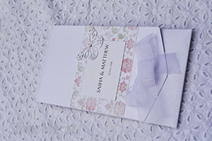 Image of Broderie Antique Rose long pocketfold invitation, decorated with flower and vine paper, organza bow , butterfly and gem.